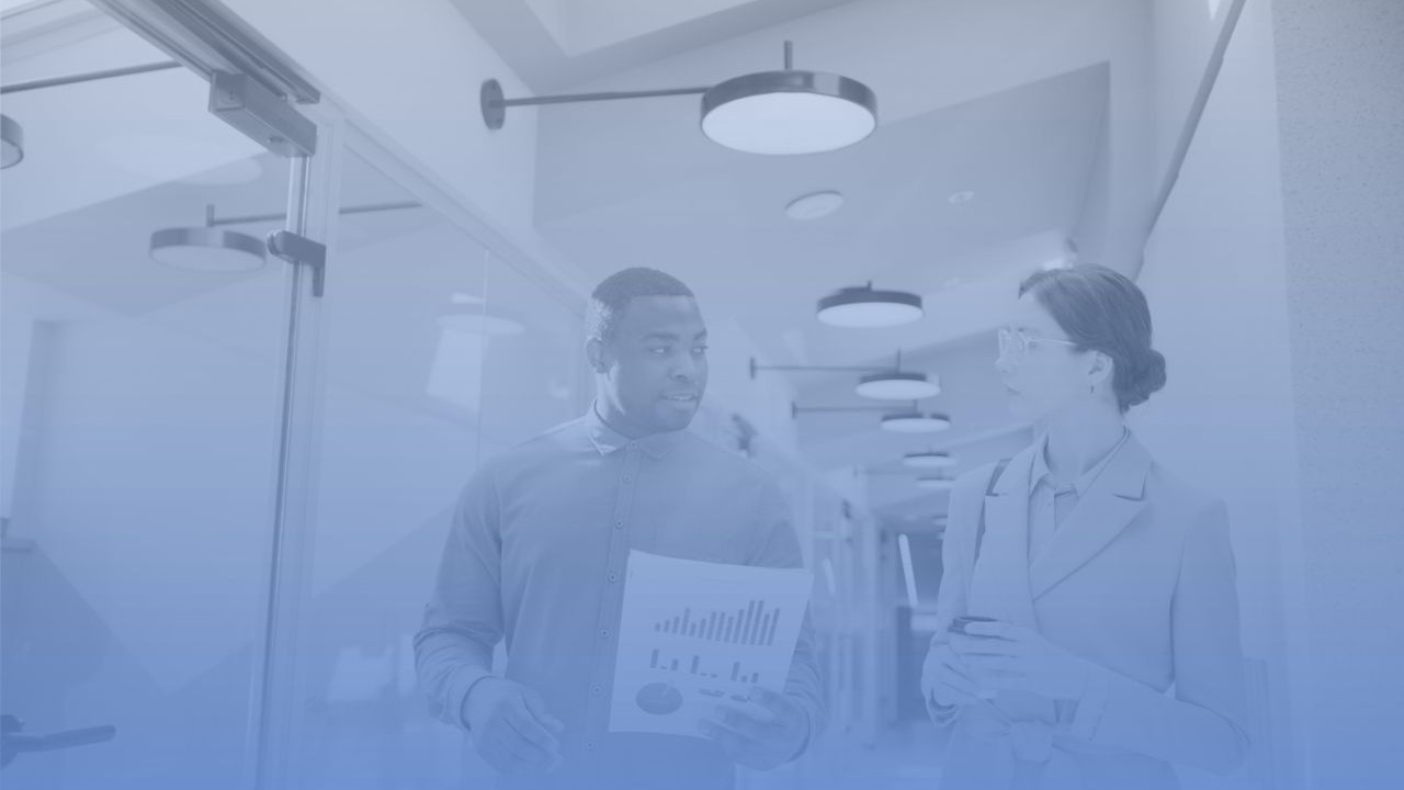 Dos personas profesionales conversando en un pasillo de oficinas modernas, una de ellas sosteniendo una hoja con gráficos de métricas de linkedIn ads